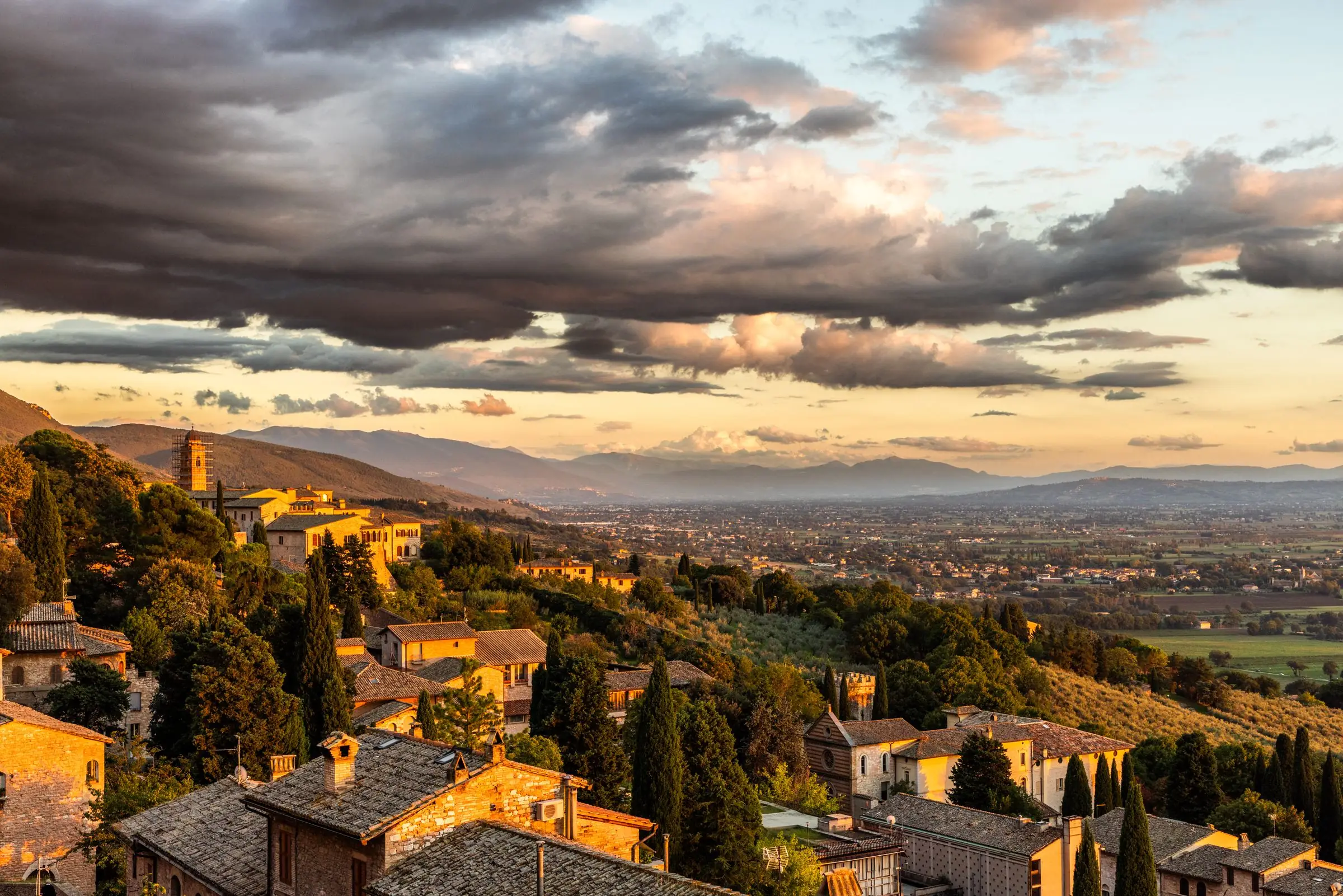Assisi e la Valle Umbra al tramonto, sotto un cielo di nuvole